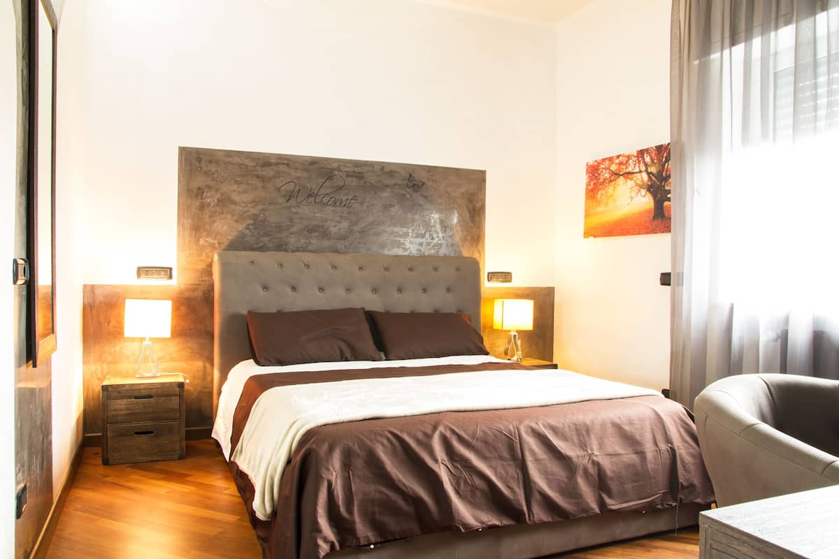 A bedroom with a large bed, two bedside tables with lamps, a headboard with a welcome sign, and a painting on the wall.