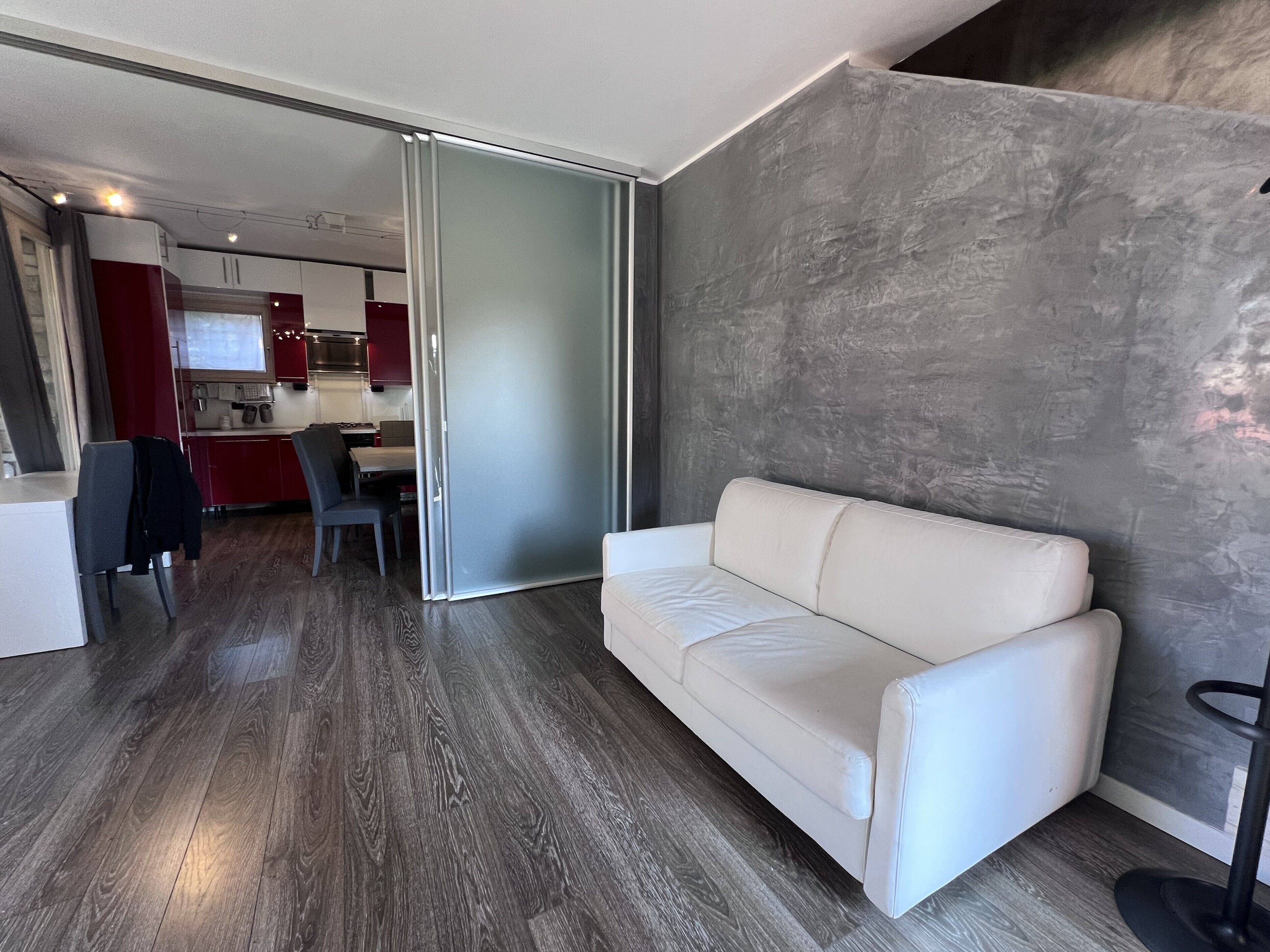 A modern living room with a white sofa, a dining area with a table and chairs, and a kitchen in the background.