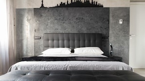 Un dormitorio moderno con una cama grande, un cabecero con silueta del horizonte de una ciudad, una mesita de noche y una mesita auxiliar.