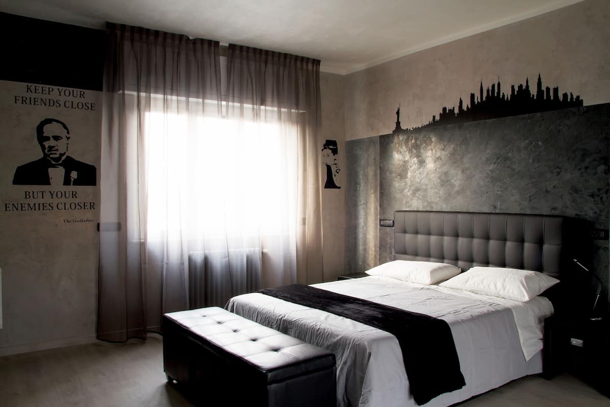 A bedroom with a large bed, a bench, a city skyline mural, and a poster with text.