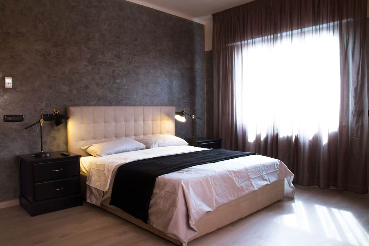 A bedroom with a large bed, two bedside tables, a nightstand, and a window with curtains.