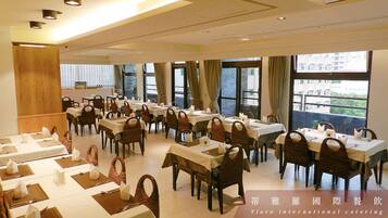 A spacious dining area with multiple tables set for meals, large windows offering views of the outside, and a modern interior design.