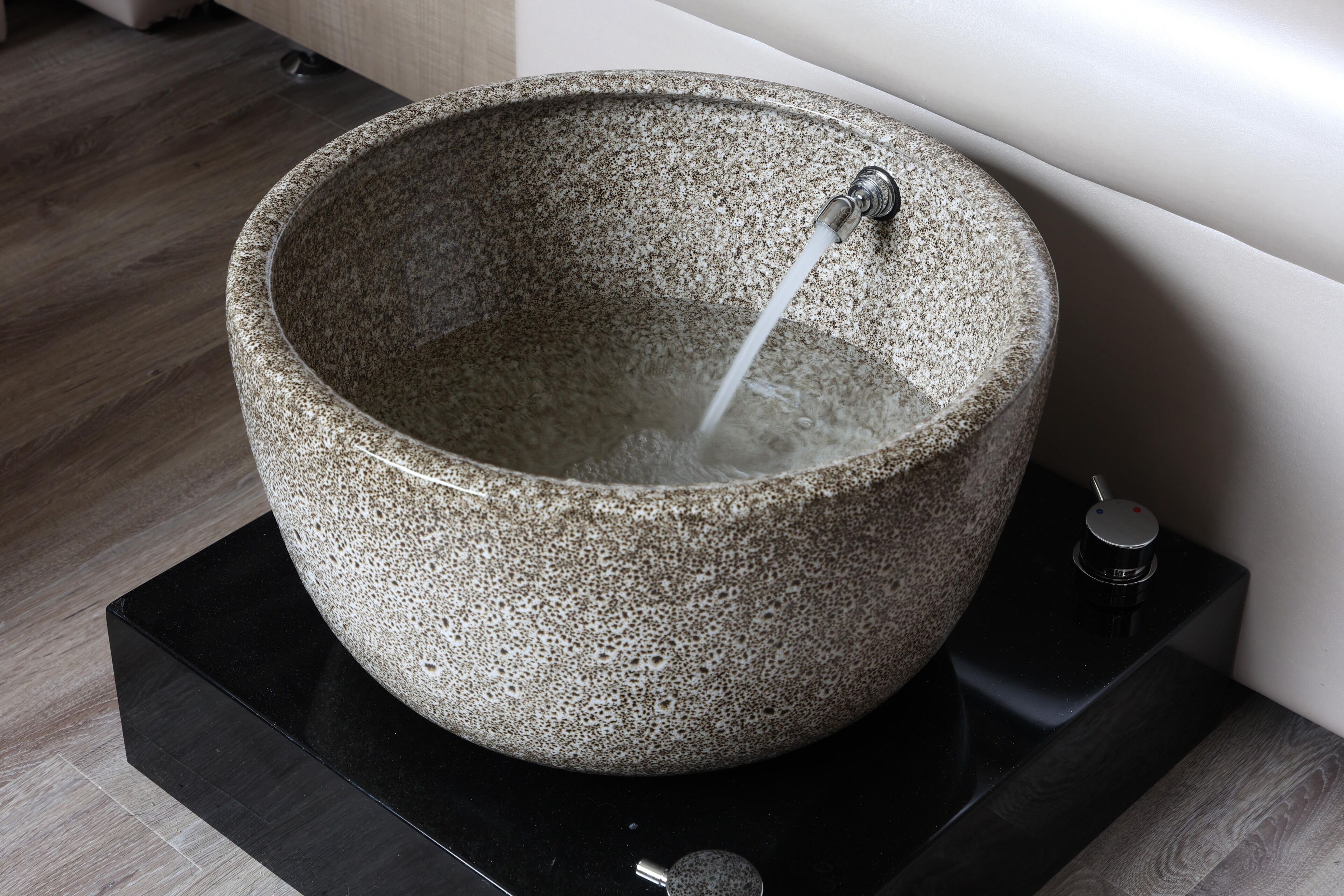 A stone basin with a faucet, placed on a black platform.
