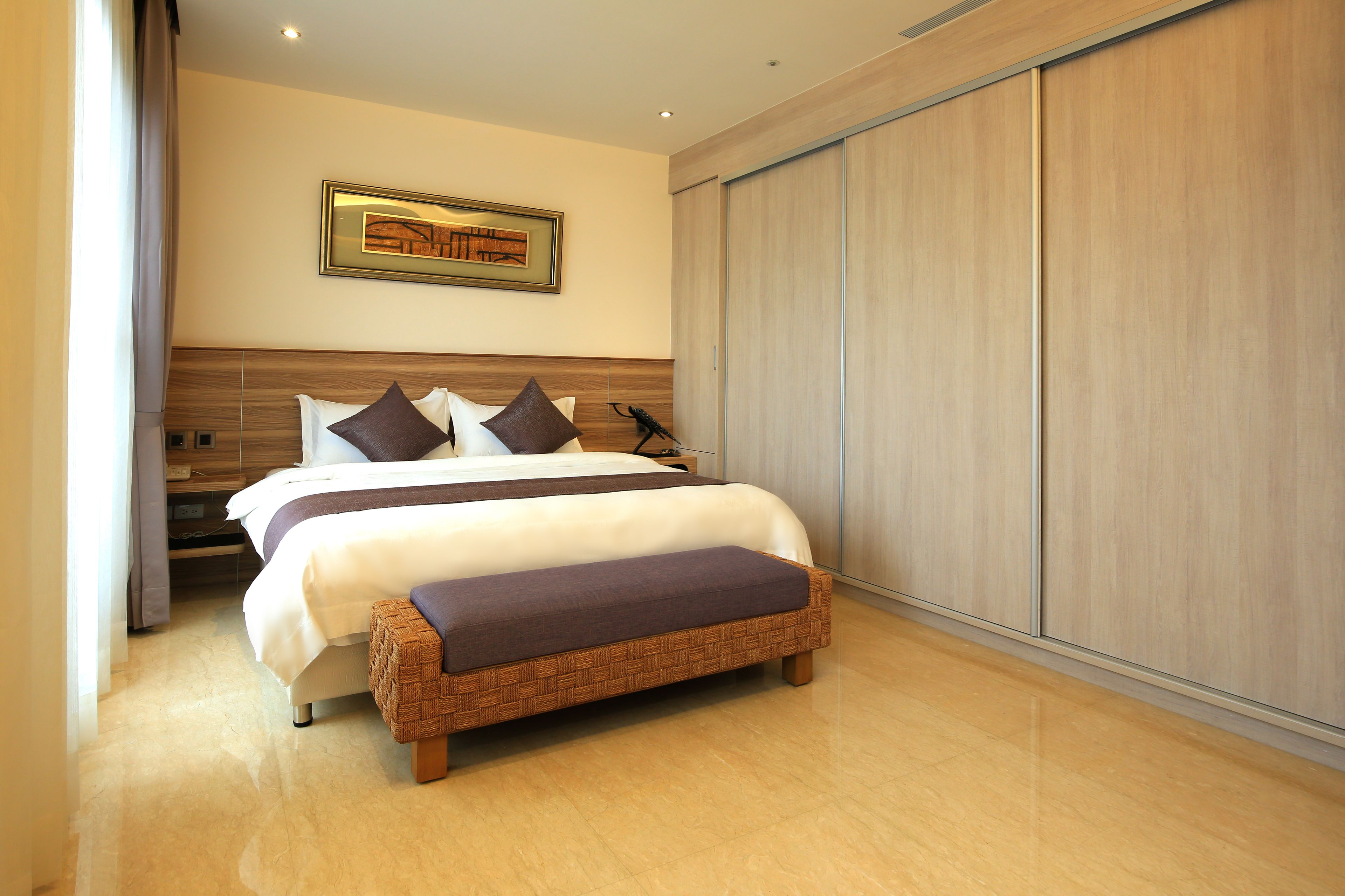 Una habitación de hotel moderna con una cama grande, una mesita de noche, una obra de arte colgada en la pared y un armario corredero.