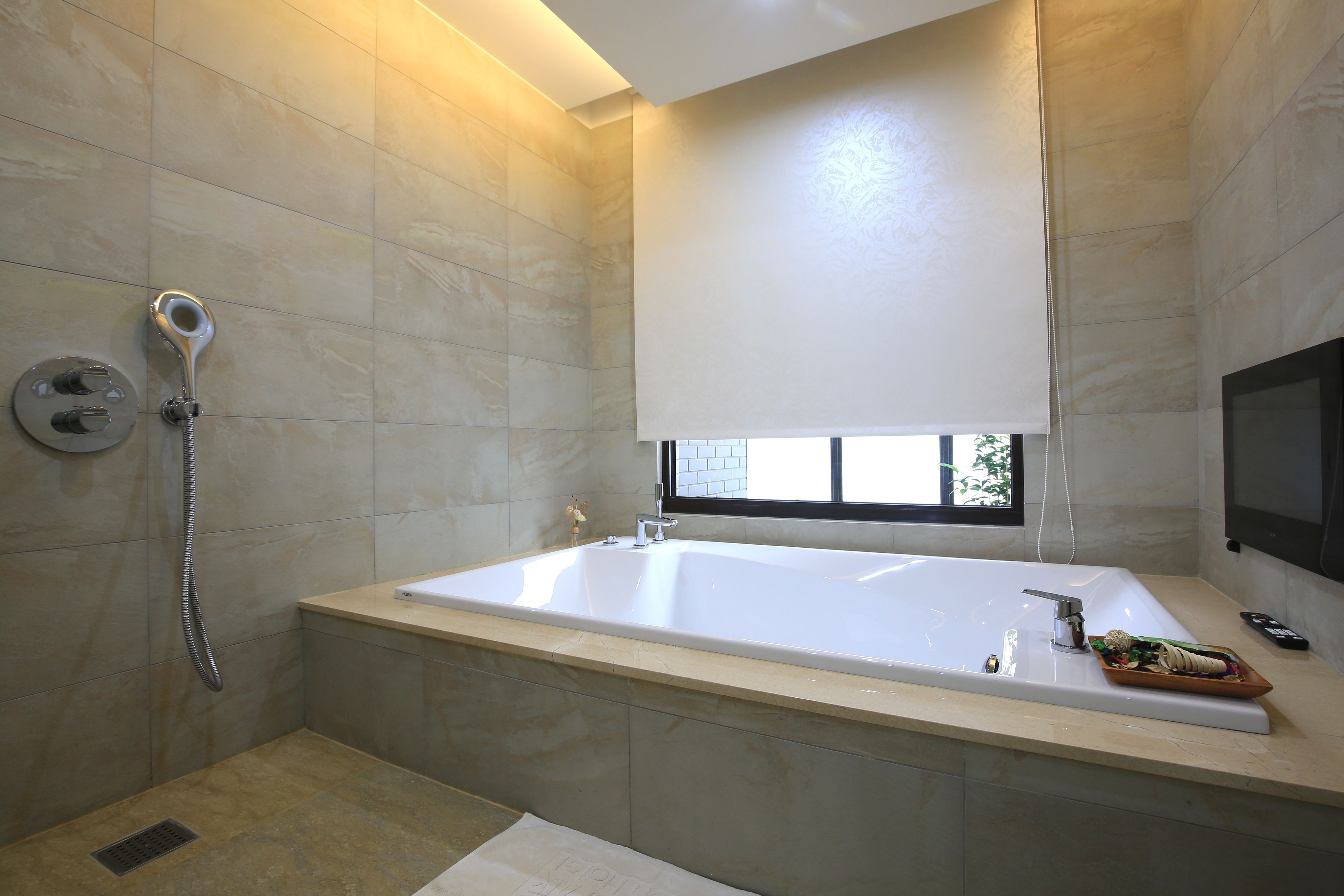 A modern bathroom with a large bathtub, a showerhead, and a window providing natural light.