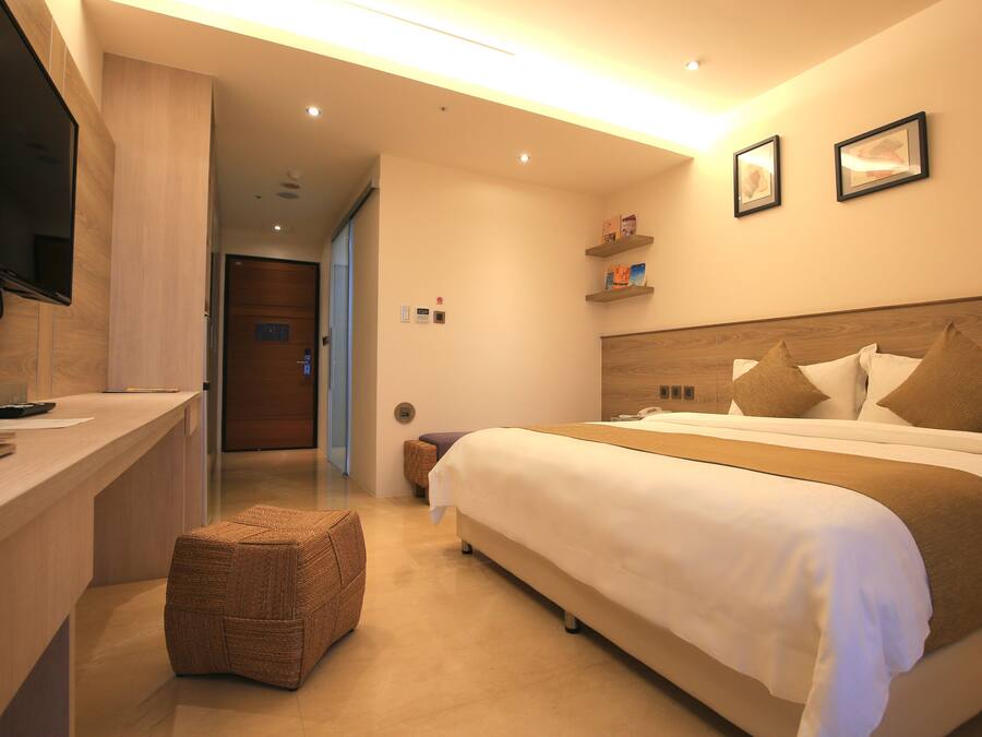 A hotel room with a bed, a desk, a television, and a small seating area.