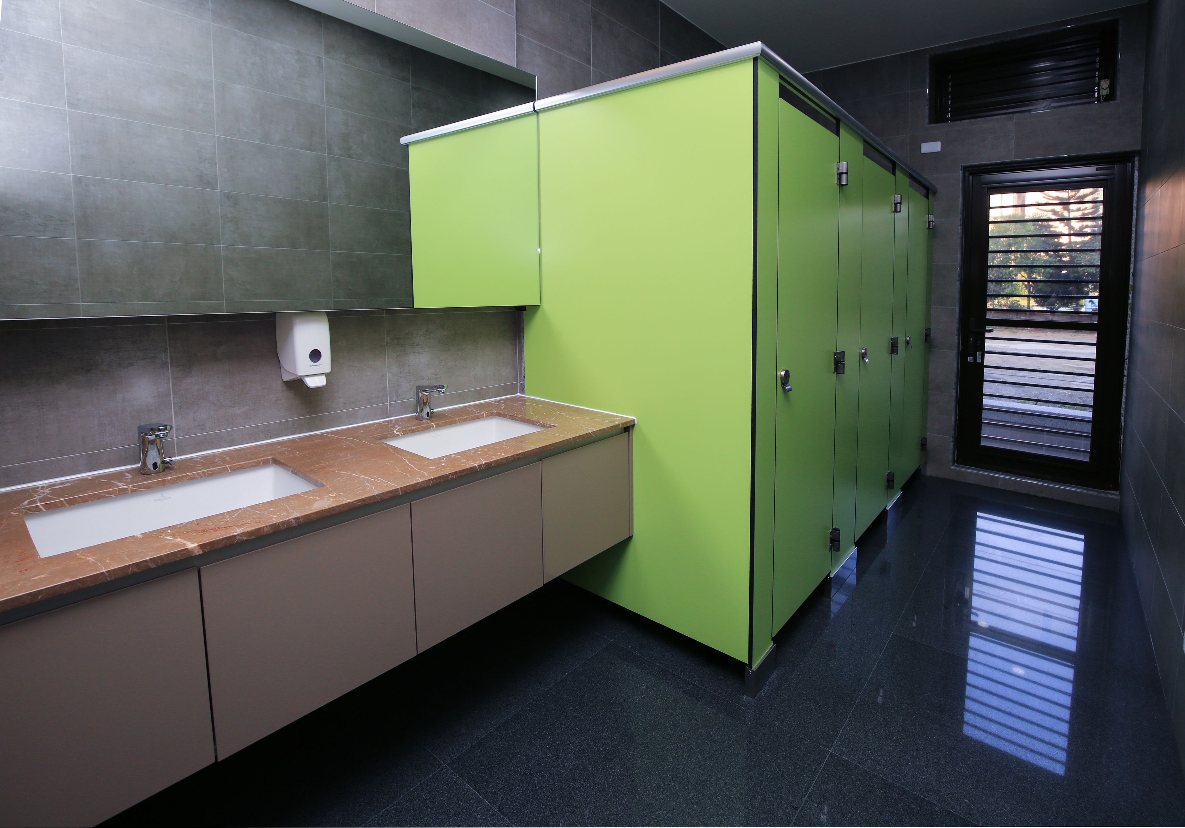 A modern bathroom with two sinks, green cabinets, and a tiled floor.