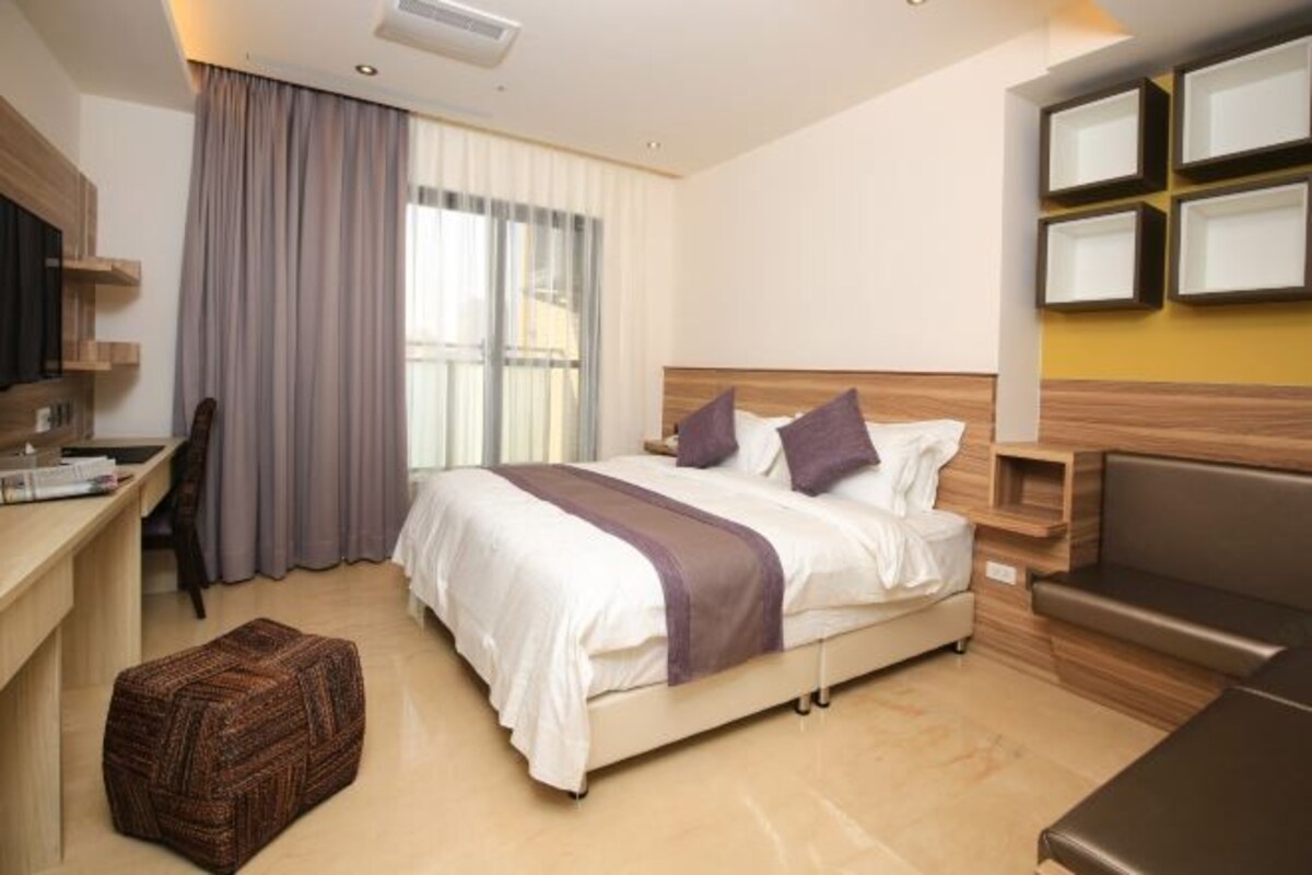 A hotel room with a bed, a desk, a chair, a TV, and a window with curtains.