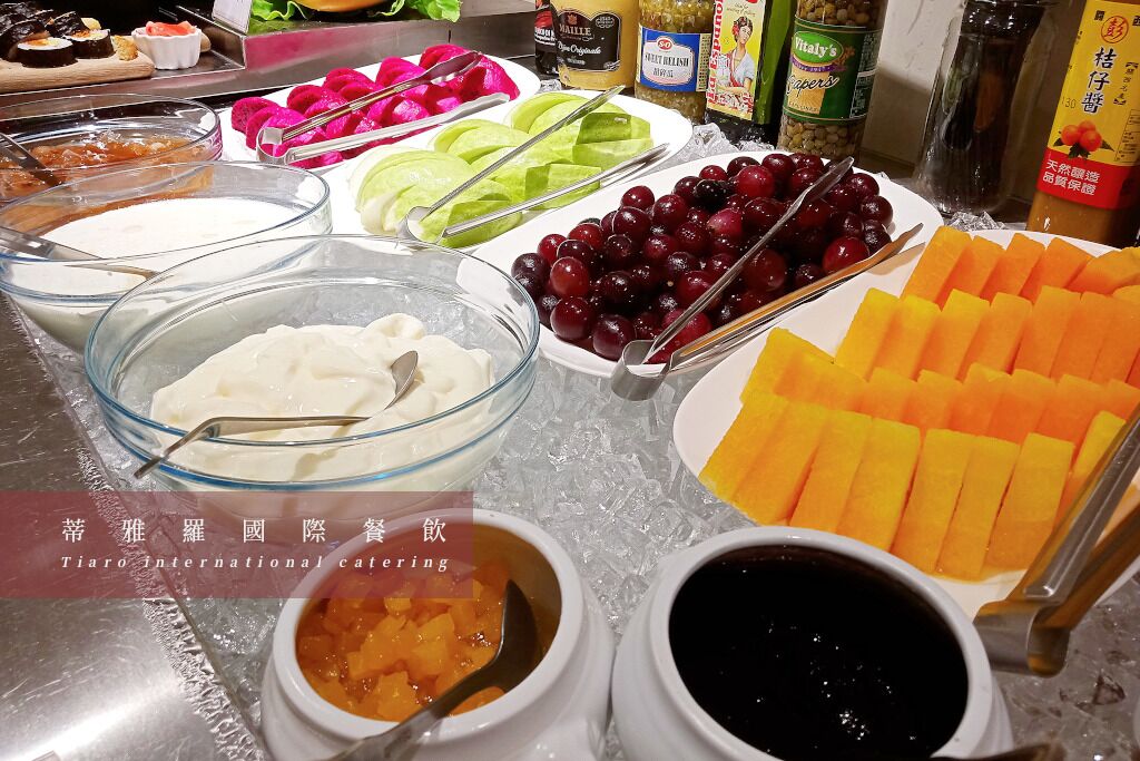 Un bufé con diversos alimentos, incluyendo frutas, verduras y salsas.