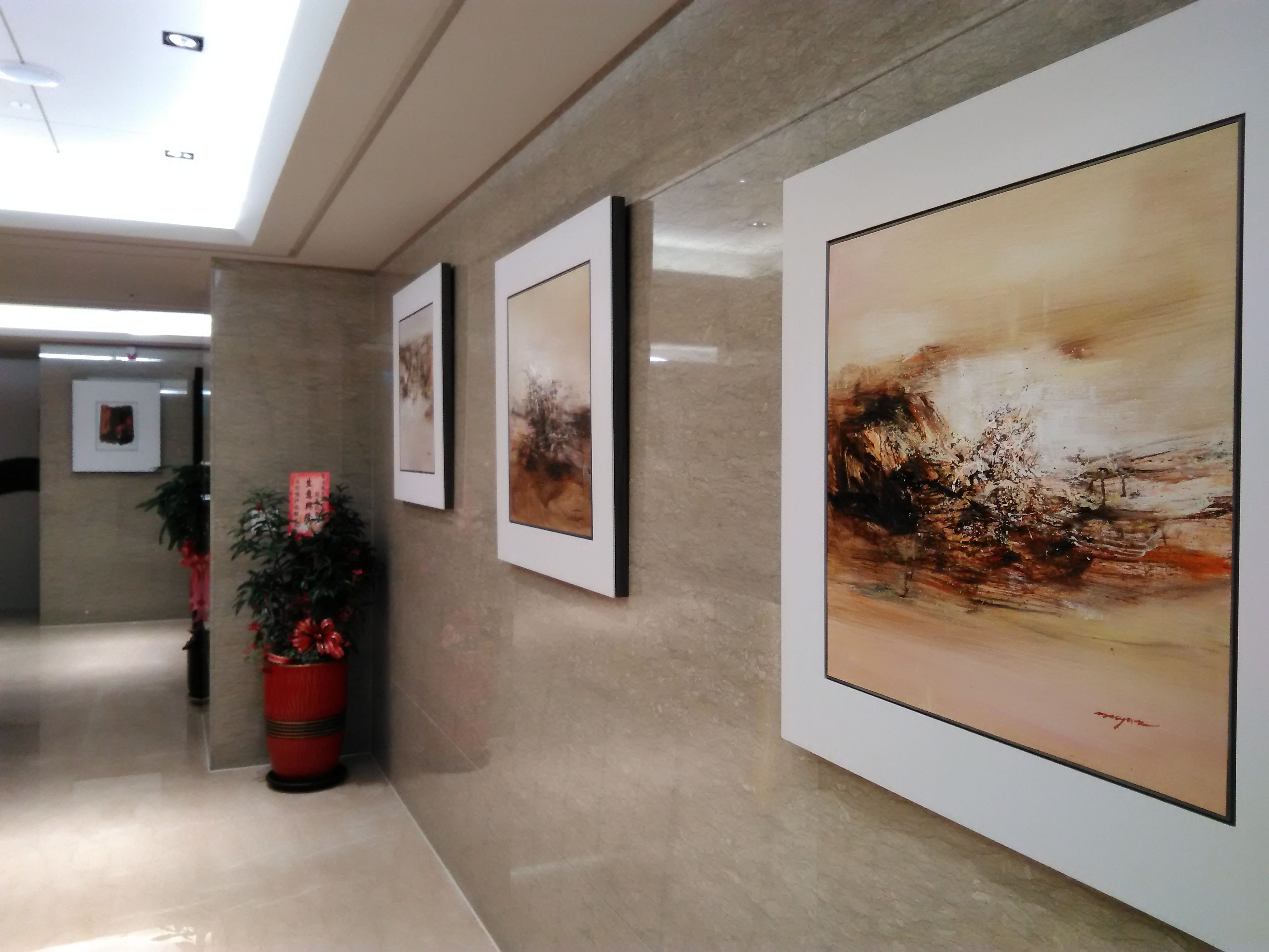 A hallway with framed artworks on the walls, potted plants, and a ceiling with recessed lighting.