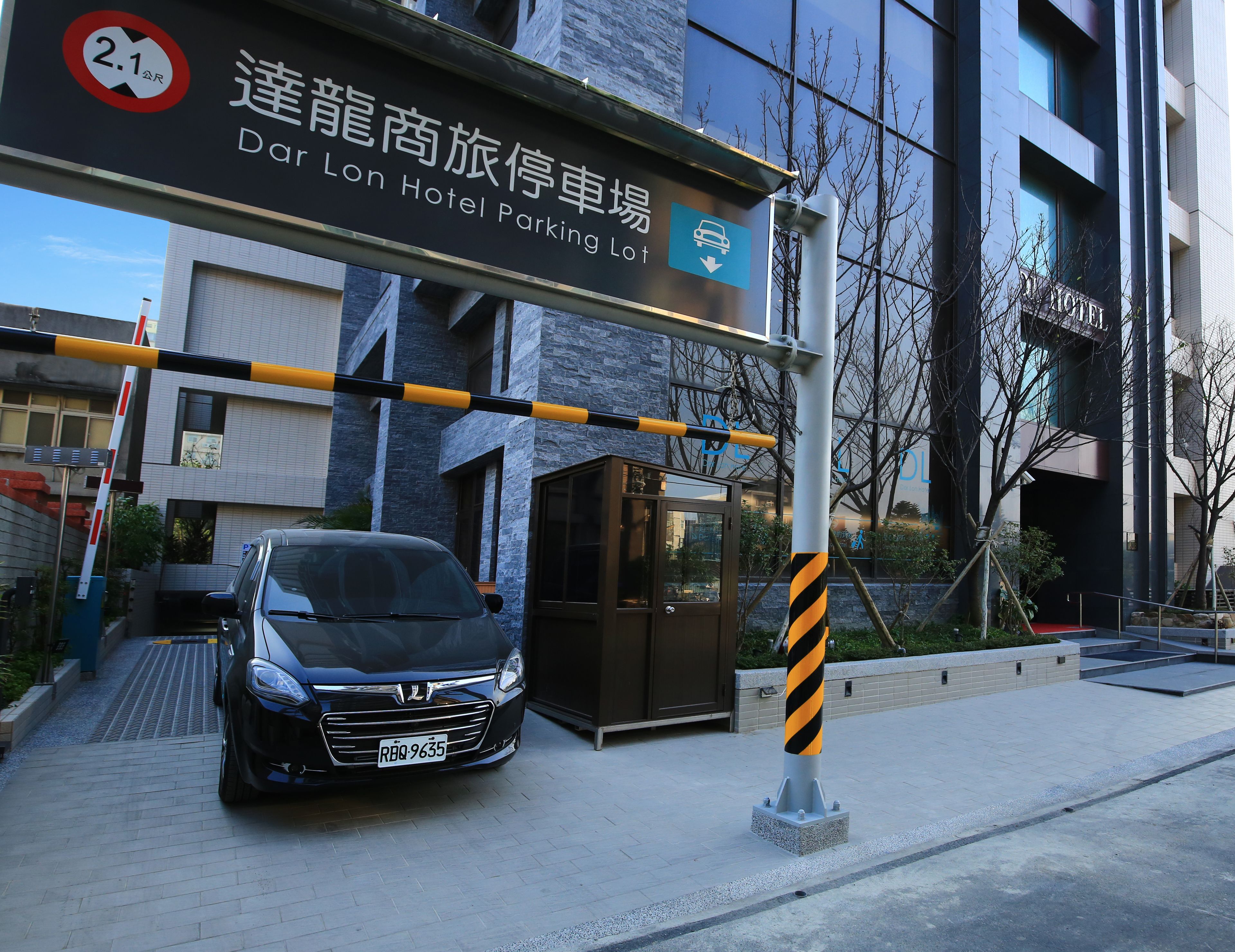 A car parked in front of Dar Lon Hotel Parking Lot with a sign indicating a 2.1 meter height limit.