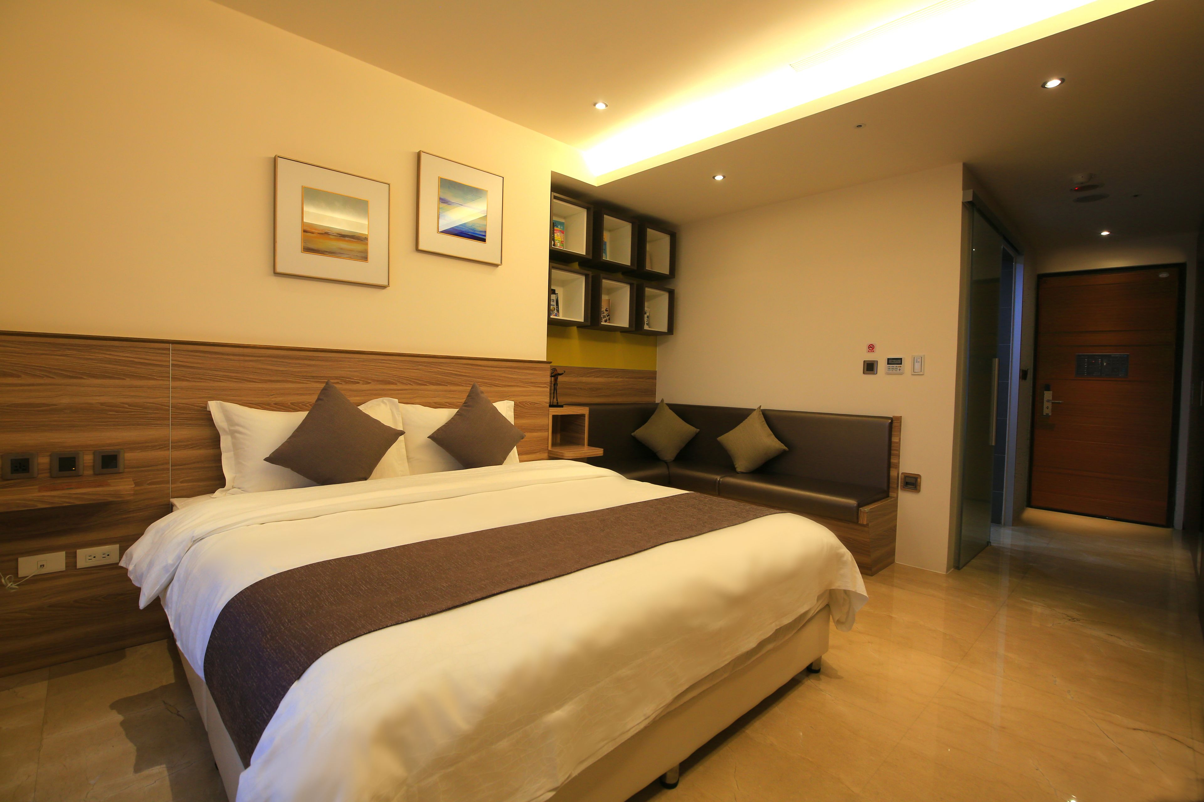 Een moderne hotelkamer met een groot bed, een houten hoofdbord, een inbouwplank en een flatscreen televisie.