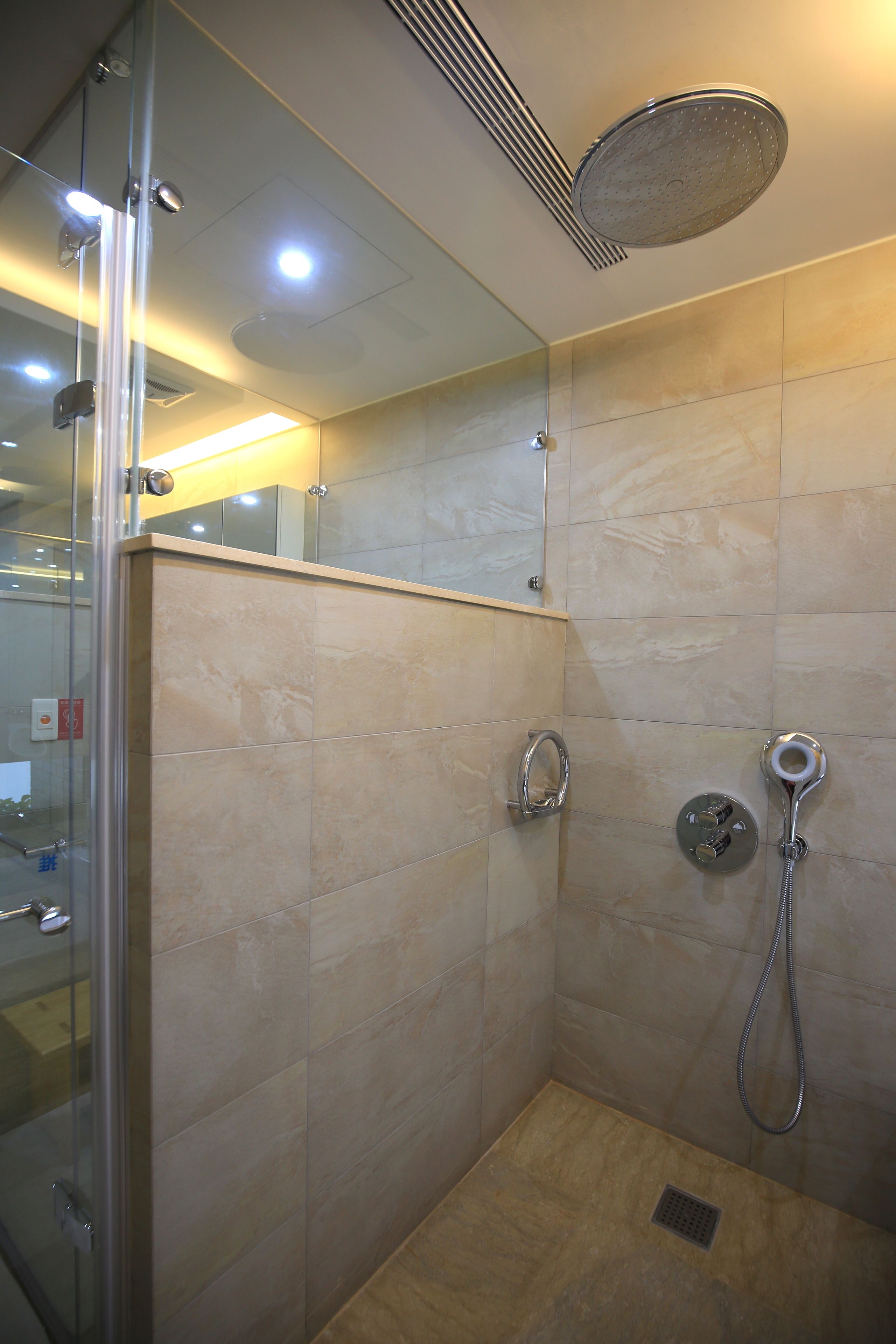 A glass-enclosed shower with a handheld showerhead and a wall-mounted faucet.