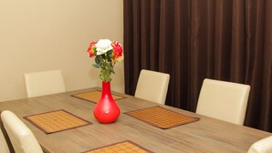 Una mesa de comedor con un jarrón rojo de flores, cuatro sillas blancas y manteles individuales marrones.