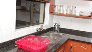 Una cocina con un lavamanos de acero inoxidable, una ventana con cortina a rayas y una encimera con escurreplatos.