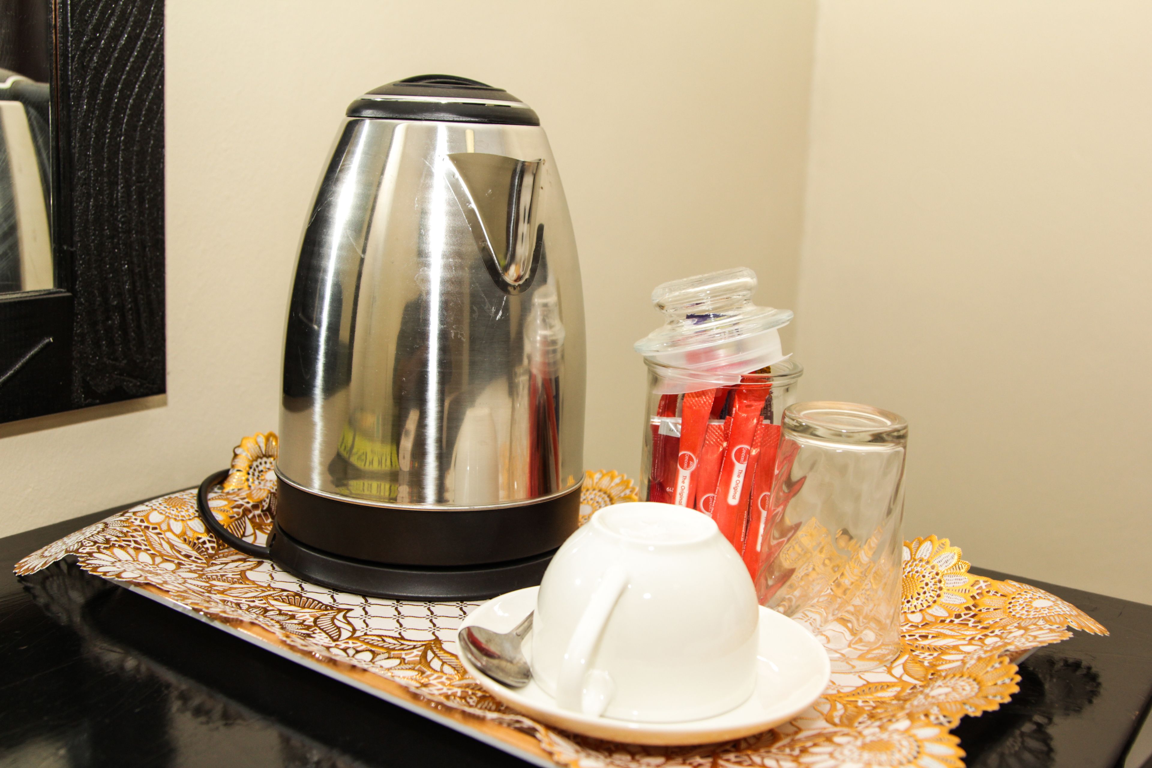 A coffee maker, a cup, and a sugar container on a table with a lace tablecloth.