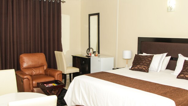 Habitación de hotel con una cama grande, un sillón de cuero, un escritorio con lámpara y un refrigerador pequeño.
