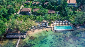 An aerial view of a resort with a clear pool, a dock, and multiple beach umbrellas. - Camia Resort & Spa (Phu Quoc)