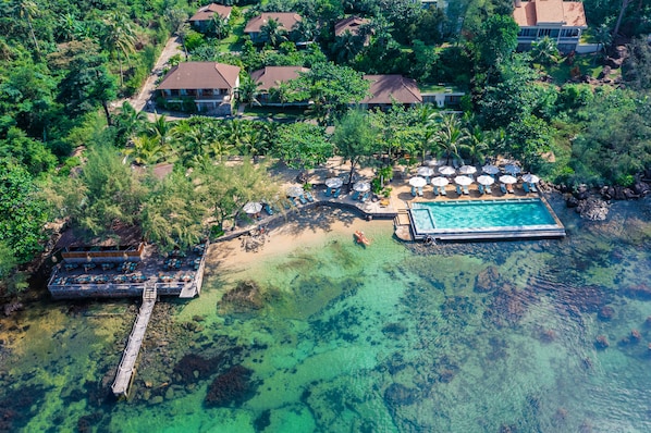 An aerial view of a resort with a clear pool, a dock, and multiple beach umbrellas. - Camia Resort & Spa (Phu Quoc)