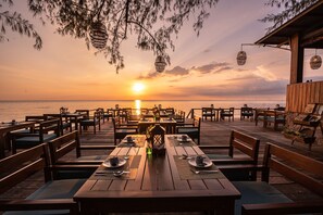 A wooden deck with tables and benches, overlooking a body of water at sunset. - Camia Resort & Spa (Phu Quoc)