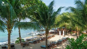 A beach resort with rows of sun loungers, palm trees, and a view of the ocean. - Camia Resort & Spa (Phu Quoc)