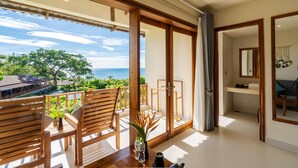 A balcony with wooden chairs and a table, a view of the ocean, and a glimpse of a bathroom with a mirror and sink. - Camia Resort & Spa (Phu Quoc)