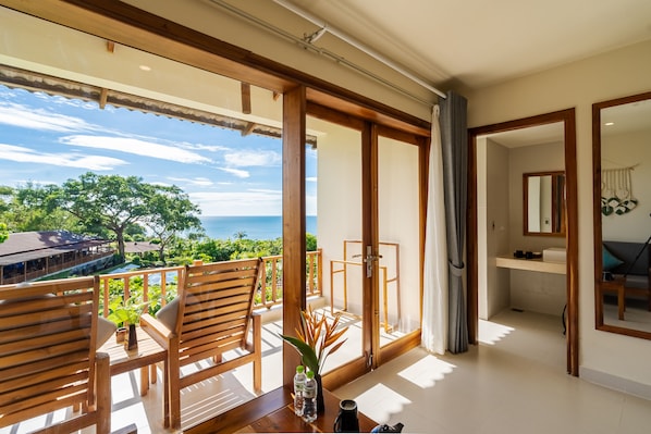 A balcony with wooden chairs and a table, a view of the ocean, and a glimpse of a bathroom with a mirror and sink. - Camia Resort & Spa (Phu Quoc)
