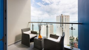 A balcony with wicker furniture, a vase with flowers, and a view of the ocean and buildings. - TUI BLUE Nha Trang (Nha Trang)