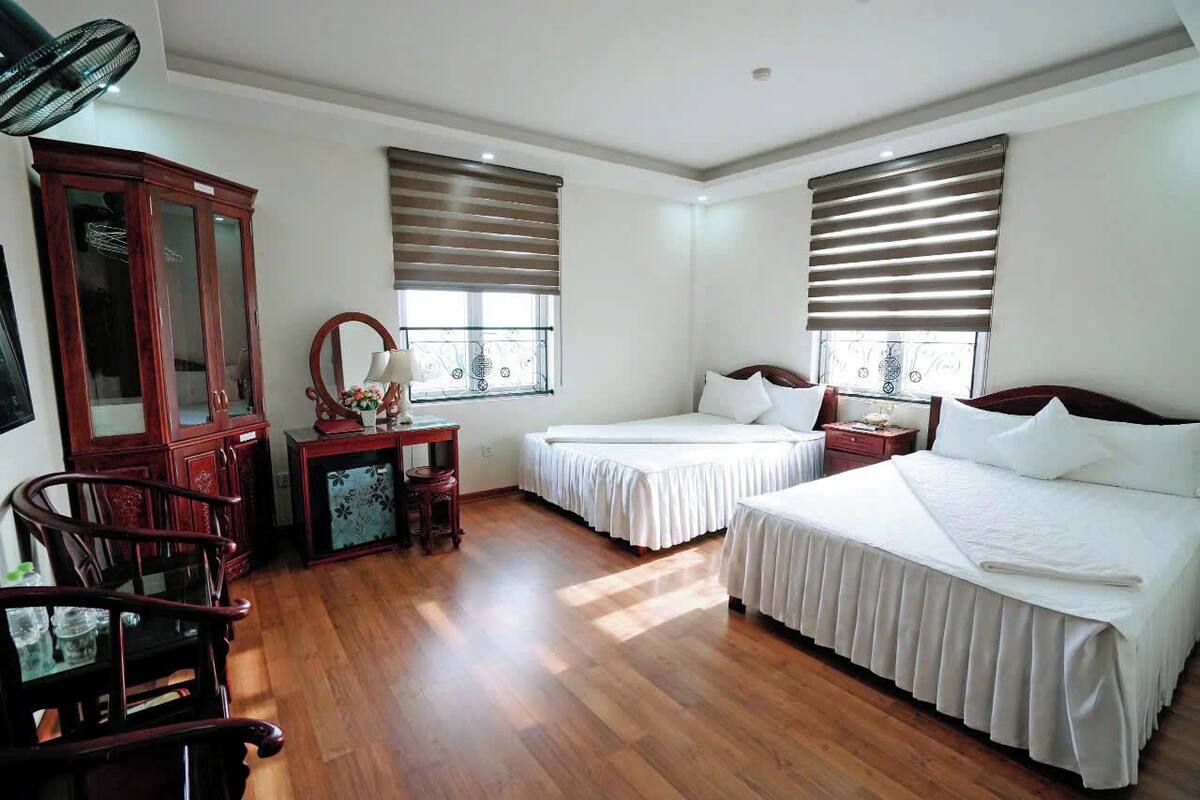 A hotel room with two beds, wooden flooring, a cabinet, and a fan.