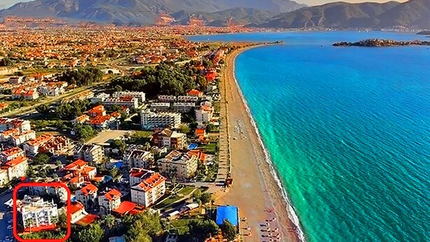 An aerial view of a coastal town with a beach, buildings, and mountains in the background. - Hotel Seril 1 (Fethiye)