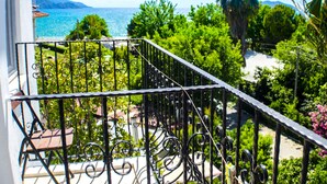 A balcony with a wrought iron railing overlooking a lush garden and a coastal view. - Hotel Seril 1 (Fethiye)