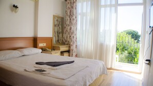 A hotel room with a bed, a bedside table with a phone, a mirror, and a window with a view of greenery. - Hotel Seril 1 (Fethiye)