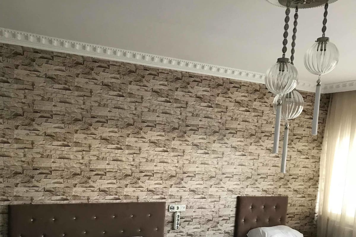 A hotel room with a brick-patterned wall, a large bed with a tufted headboard, a smaller bed, and a hanging light fixture.