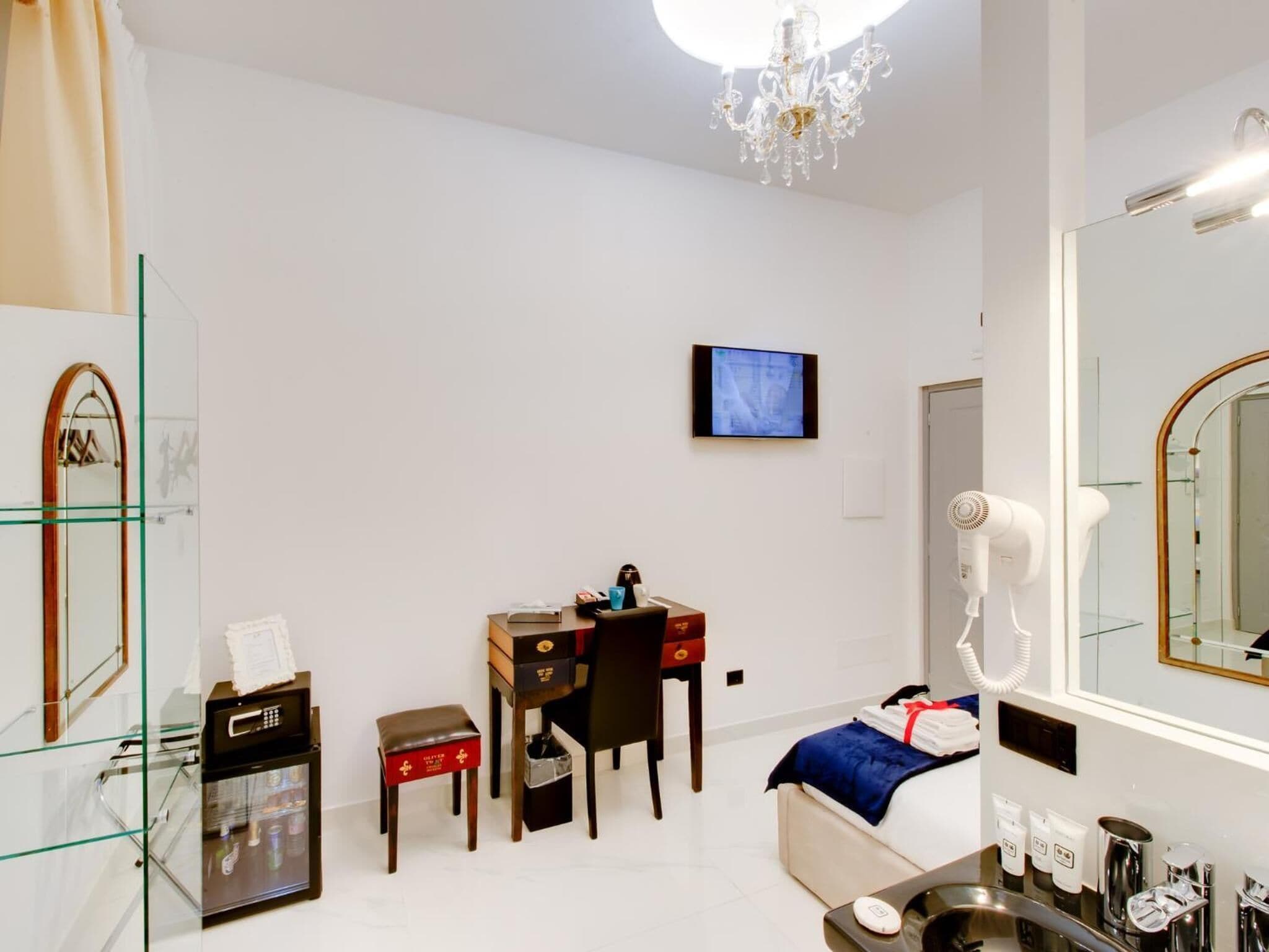 A hotel room with a desk, chair, television, hairdryer, and a large mirror.