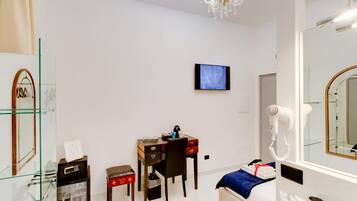 A hotel room with a desk, chair, television, hairdryer, and a large mirror.