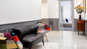 A modern living room with a black leather sofa, colorful cushions, a wooden side table, and a vase with flowers. - Queen Palace Suites (Rome)
