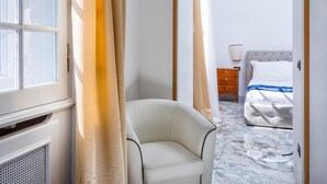 A hotel room with a marble floor, a bed with white bedding, a wooden nightstand, and a chair. - Queen Palace Suites (Rome)