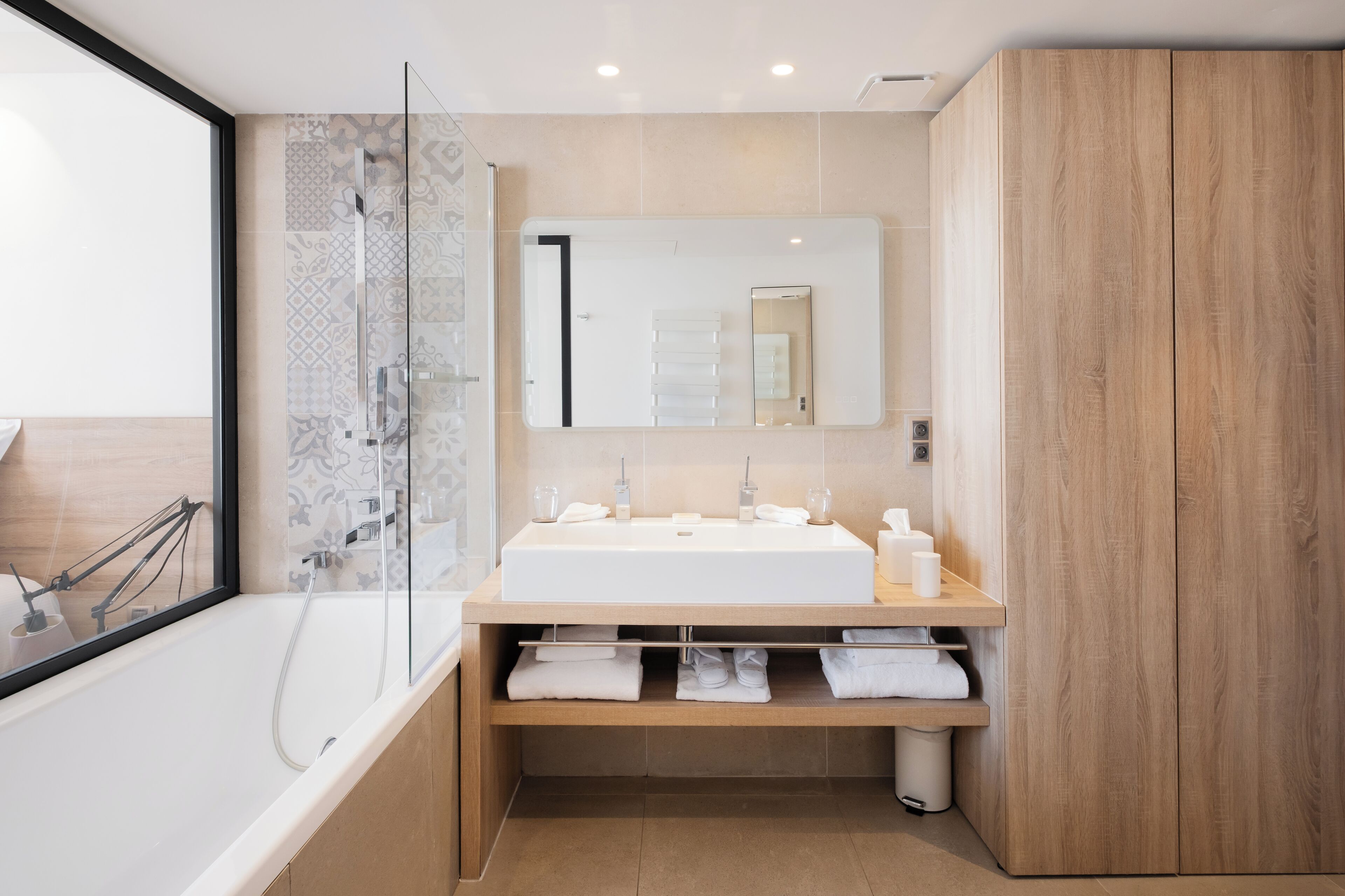 A modern bathroom with a glass shower enclosure, a large mirror, and a wooden vanity with a sink.