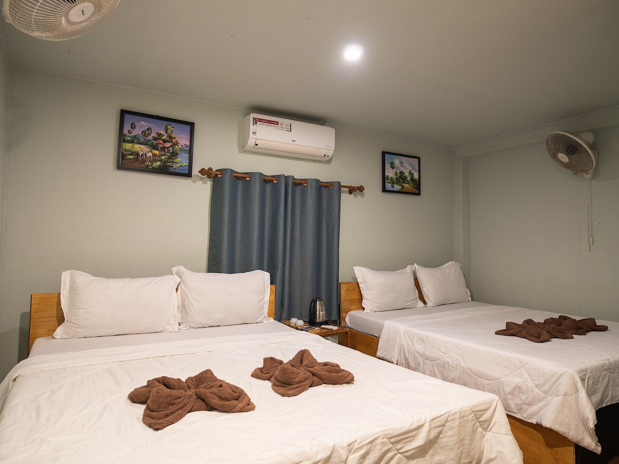 A hotel room with two beds, a ceiling fan, an air conditioning unit, and two framed pictures on the wall.