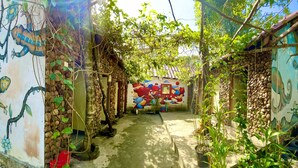 A narrow outdoor corridor with stone walls, a mural, and potted plants. - The Cliff Hostel (Koh Rong Sanloem)