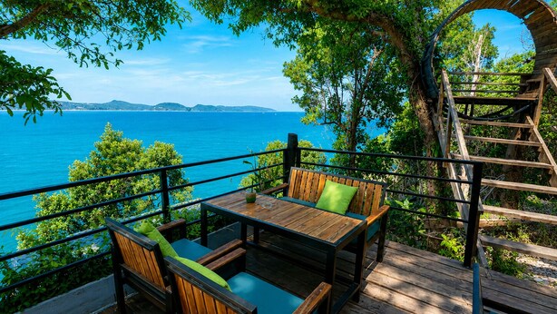 A wooden deck with a table and chairs, overlooking a body of water and distant land. - The Cliff Hostel (Koh Rong Sanloem)