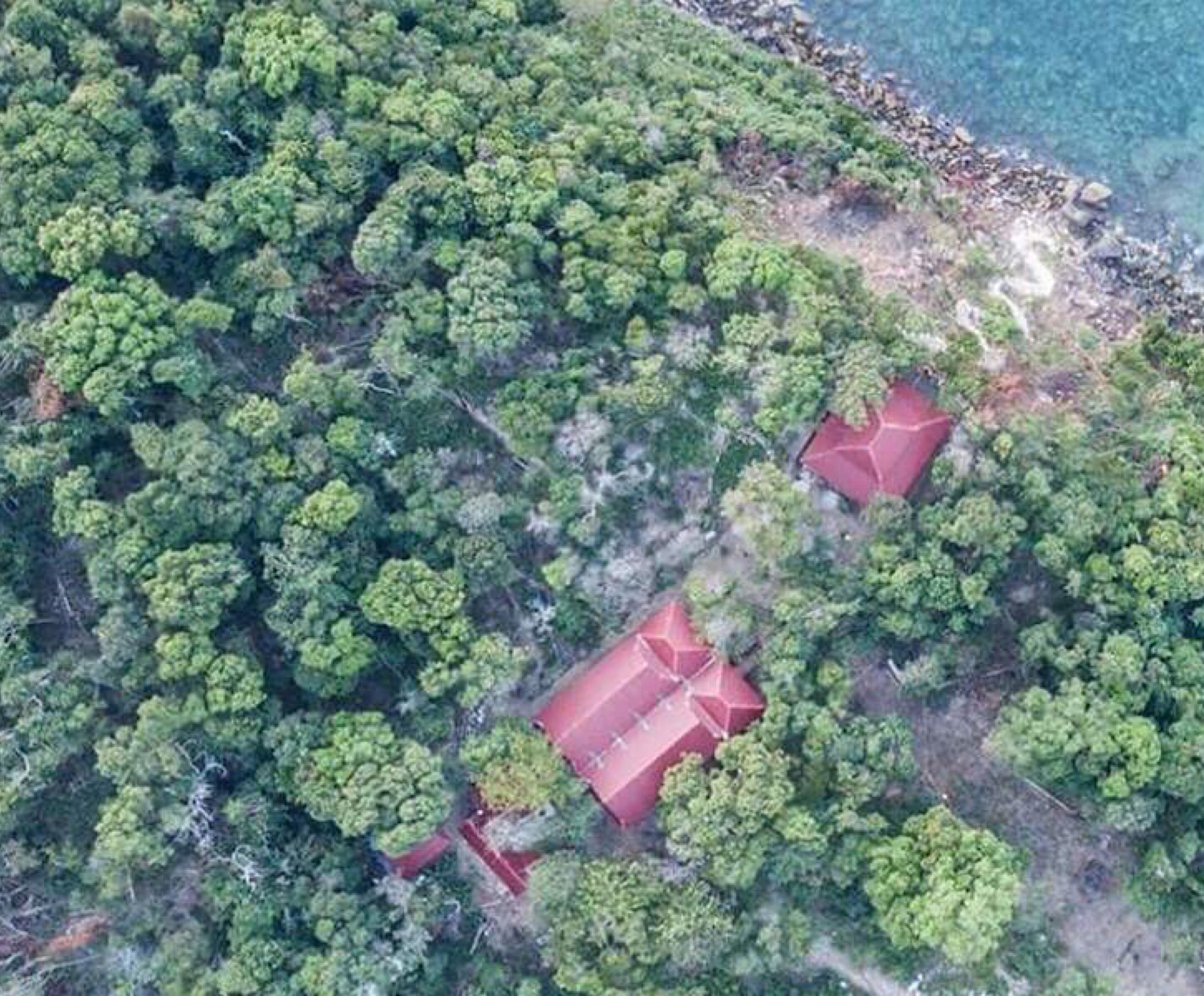 Une vue aérienne d’une propriété entourée d’une forêt dense, où l’on aperçoit deux bâtiments dont les toits sont rouges.
