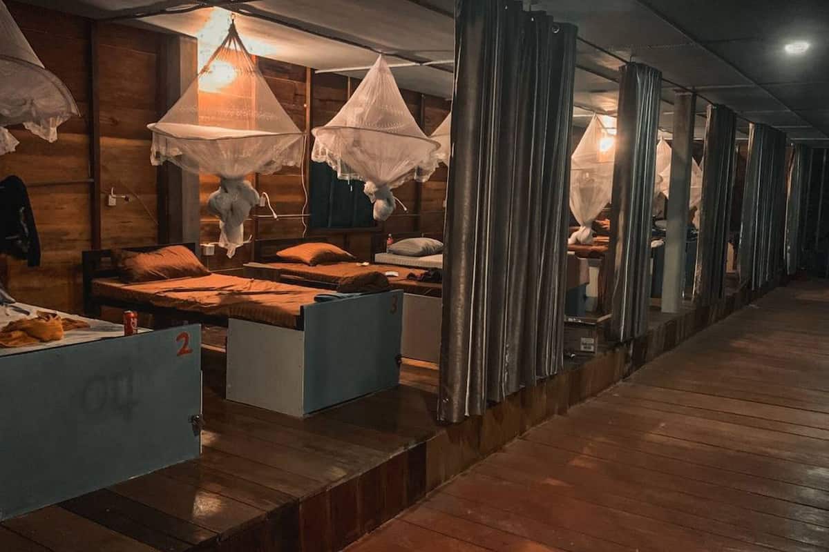 A hotel room with wooden floors, multiple beds, and hanging lamps.