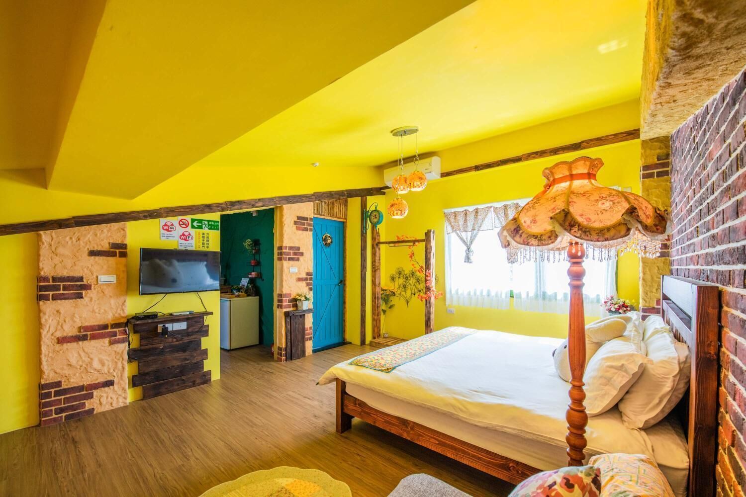 A bright yellow room with a large bed, a TV, and a brick wall.