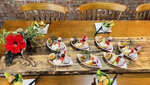 A wooden dining table with plates of fruit and vegetables, surrounded by chairs. - Cat Sky Country Homestay (Sanxing)