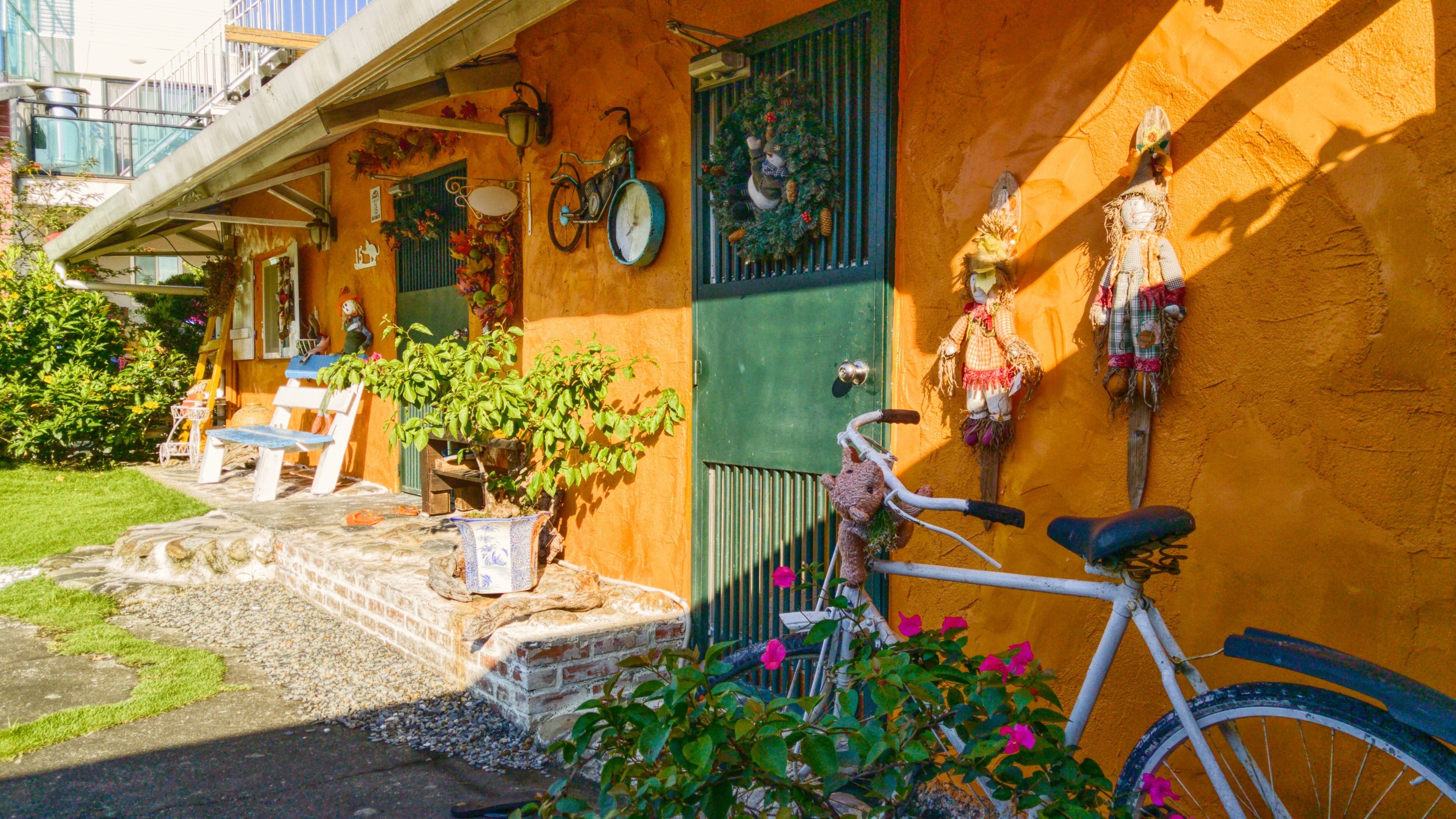 Um edifício com porta verde, uma bicicleta e mesas ao ar livre.