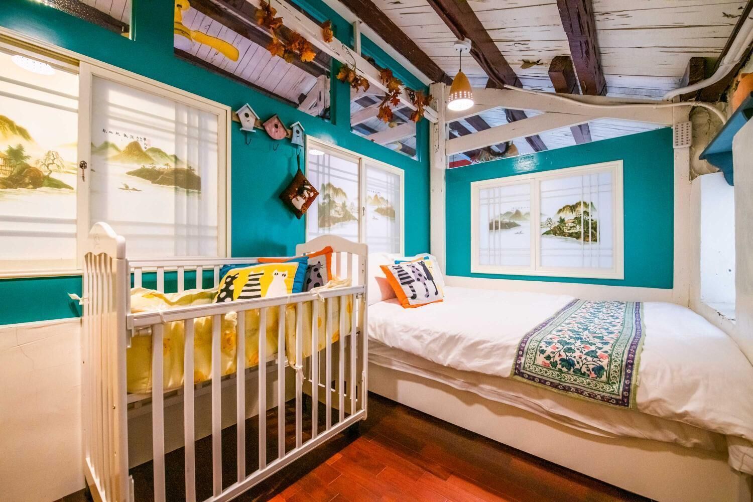 A cozy room with a crib, a small bed, and a window with a view of the sea.