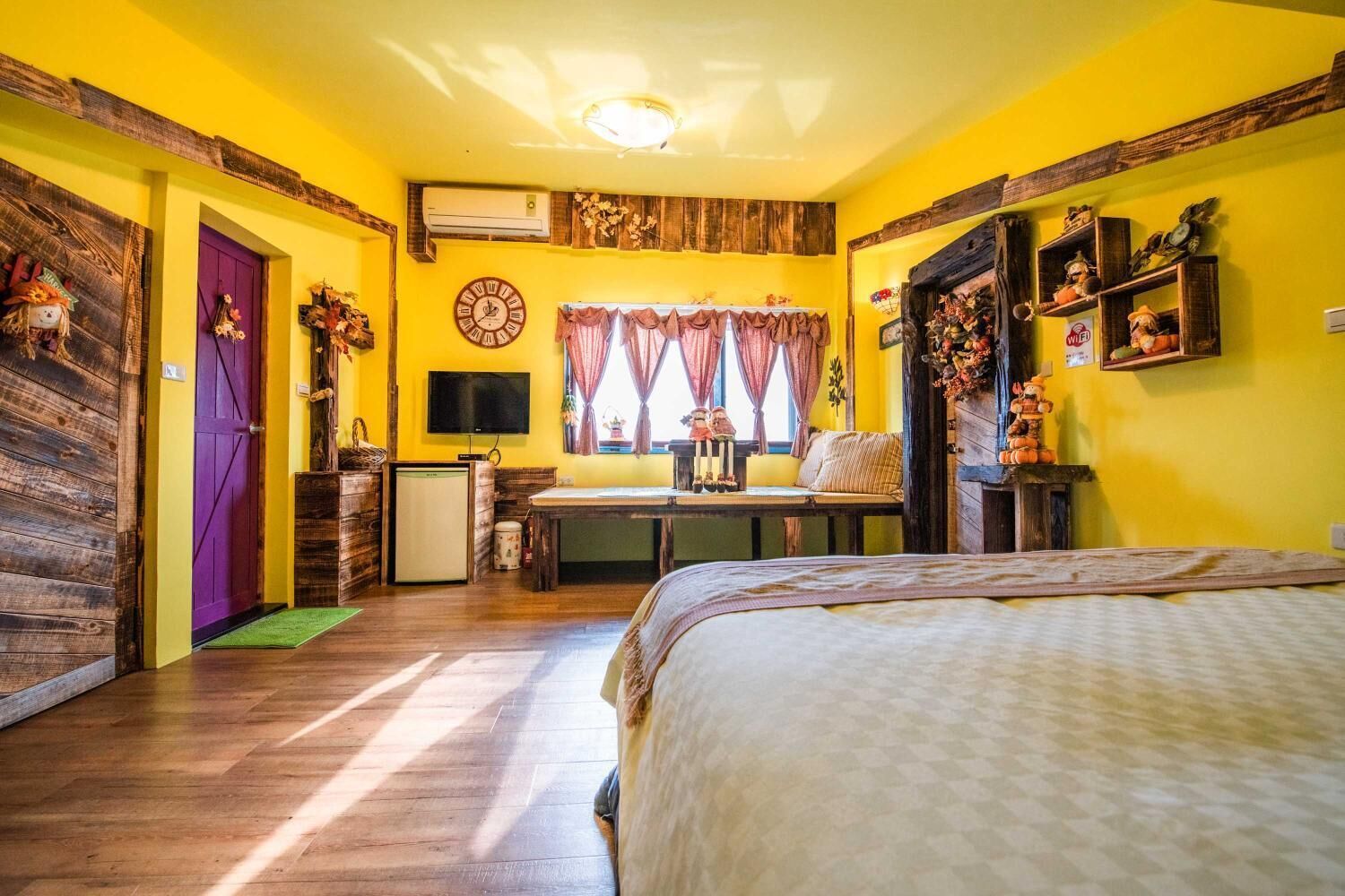 Um quarto aconchegante com uma cama, uma mesinha, uma TV e uma janela com cortinas.