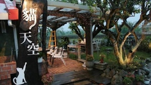 A covered outdoor seating area with a brick floor, surrounded by potted plants and a large tree. - Cat Sky Country Homestay (Sanxing)