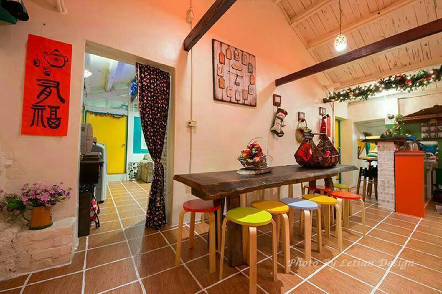 A kitchen with a wooden table and colorful stools, a red sign, and a decorative wall hanging.
